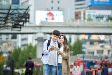 During the trip, a college student couple is looking for their way with a map at Seoul Station during the day.