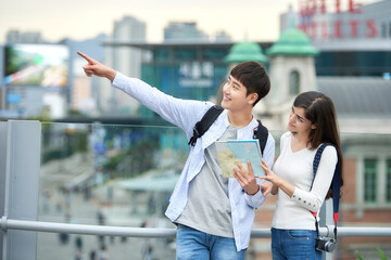 During the trip, a college student couple is looking for their way with a map at Seoul Station during the day.