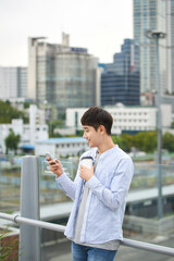 A young man is resting on a land bridge with coffee and a smartphone in the background of a busy...