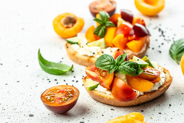Fototapeta na wymiar Open sandwiches with cream cheese, peaches, tomatoes and green basil leaves on a light background, Long banner format. top view