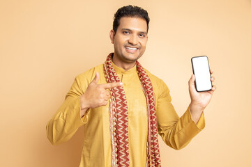 Happy young handsome indian man wearing traditional kurta holding smart phone with blank display...
