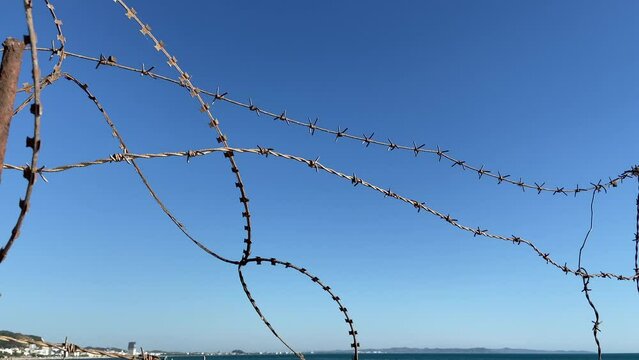barbed wire barrier against the sea and blue sky background. barb wire fence over blue sky and sea