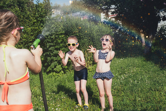 Children in swimsuits play with a garden hose on a hot summer day. Siblings splashing water outdoors. Childhood, leisure on weekends and holidays. International Children's Day concept