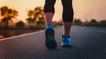 Rear view of a man's feet before running. Adult man doing exercise running and walking on country road in the morning with sunrise background. Concept of health and lifestyle.