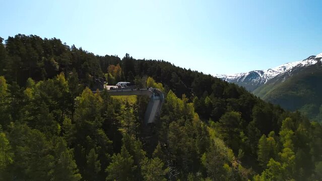 Drone footage around Stegastein viewpoint with green forested hill on a sunny day