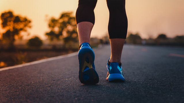 Rear View Of A Man's Feet Before Running. Adult Man Doing Exercise Running And Walking On Country Road In The Morning With Sunrise Background. Concept Of Health And Lifestyle.