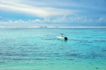 Naklejka premium Motorboat sailing towards the horizon in the blue sea against the cloudy blue sky