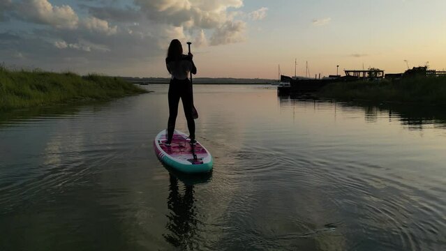 Drone footage of a woman on stand up paddle board on the sea with a sunset orange sky