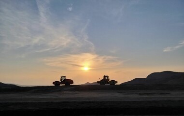 Two industrial vehicles parked on top of a hill with a beautiful sunset in the background