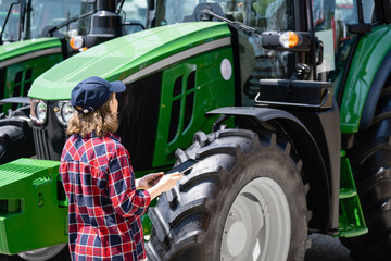 Woman farmer with a digital tablet on the background of an agricultural tractors.