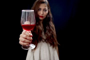 Red wine glass in hand of beautiful black long hair woman white ghost spooky costume in dark background, scary dead corpse female holding wine glass to celebrate Halloween party night.