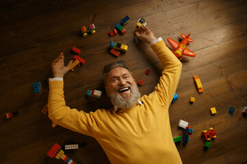 Happy senior man lying on floor with scattered toy building blocks