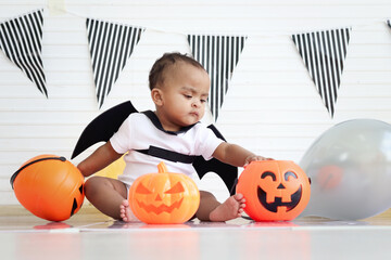 Cute African baby kid dressing up vampire fancy Halloween costume with black bat wings, cheerful little cute child holds Halloween pumpkin to play trick or treat at party. Happy Halloween celebration.