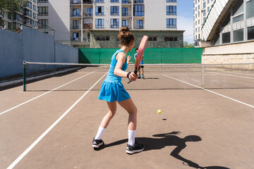 Unrecognizable young girl playing tennis ball with padel bat with anonymous teenage boy