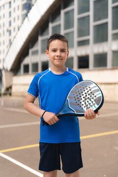 Happy young boy standing with padel racket on sports ground near building