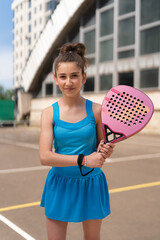 Happy young girl standing with padel racket on sports ground near building