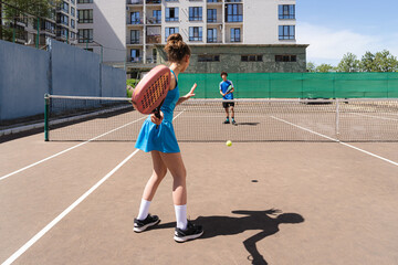 Anonymous young girl playing tennis ball with padel bat with teenage boy