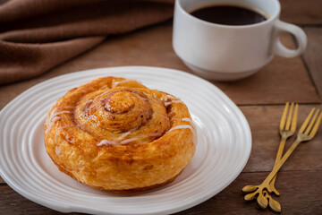 Cinnamon roll bun on white plate and cup of coffee