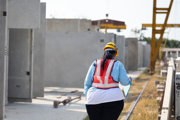 Back view Portrait African american woman. Plus size female factory worker wearing safety hard hat helmet working at heavy Prefabricated concrete walls manufacturing factory