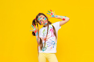 A happy little girl painted with colorful paints. Children's artistic creativity. Painted palms of the hands. A child on a yellow isolated background.