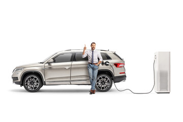 Full length portrait of a man with a SUV plugged into an electric vehicle charging station - obrazy, fototapety, plakaty