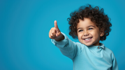 Child wearing casual clothes pointing with hand and finger to the side looking at the camera.