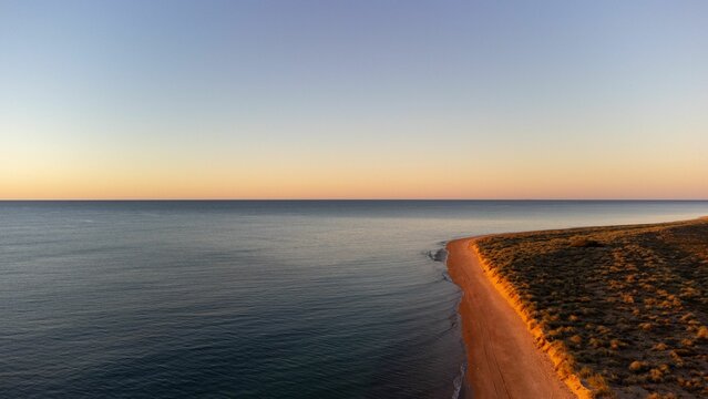 Tranquil aerial scene of a sandy beach at sunset, illuminated by a warm orange glow