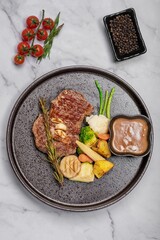 Top view of a gourmet dish with steak, vegetables and gravy on a marble table