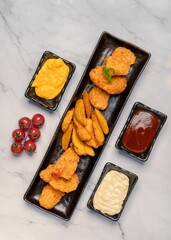 Top view of a platter of fried meat and potatoes near bowls of condiments