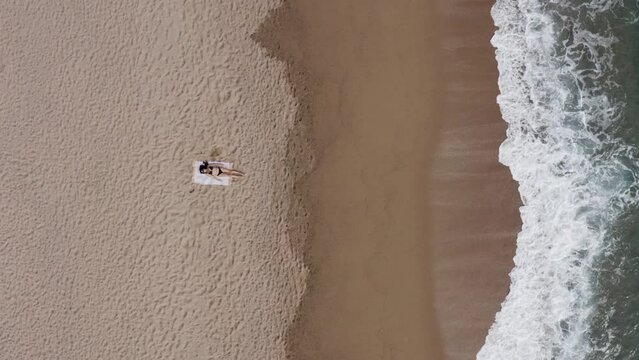 Aerial view of a female laying on a sandy seacoast with foamy waves