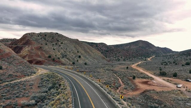 Srone footage over asphalt road between rocky cliffs and desert plants with gray cloudy sku