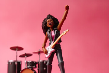 Fototapeta na wymiar Miniature people figurine of female with curly hair and raises hand playing guitar on pink background