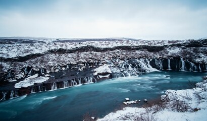 Wintery scene in Reykjavik, Iceland featuring a tranquil stream flowing between snow-covered rocks