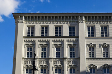 Obraz premium white wood windows in classic old exterior elevation. decorative trims. stucco facade closeup detail. flat frontal view. old european architecture. rentable office space. blue sky and white clouds