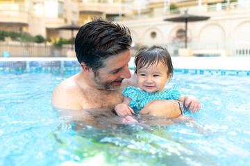 lifestyle portrait of father and little daughter enjoying summer - man holding her sweet baby girl excited and cheerful playing together at resort swimming pool in parenting concept