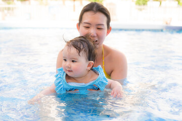 Fototapeta na wymiar happy and beautiful Asian woman holding her little baby girl playful - Korean mother and adorable daughter playing on water at resort swimming pool in Summer