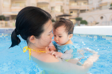 happy and beautiful Asian woman holding her little baby girl playful - Korean mother and adorable daughter playing on water at resort swimming pool in Summer