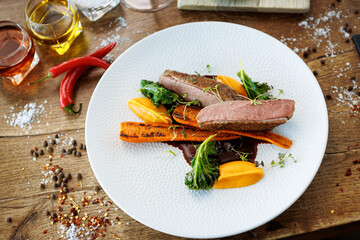 Duck fillet with sweet potato cream, roasted carrots, kale, beet-port sauce on white plate. Grilled and roasted poultry closeup served on a table for lunch in modern cuisine gourmet restaurant.