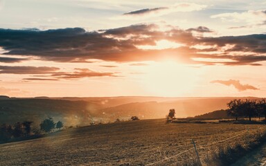 Beautiful summer evening with the sun setting behind a hillside and fields in the foreground.