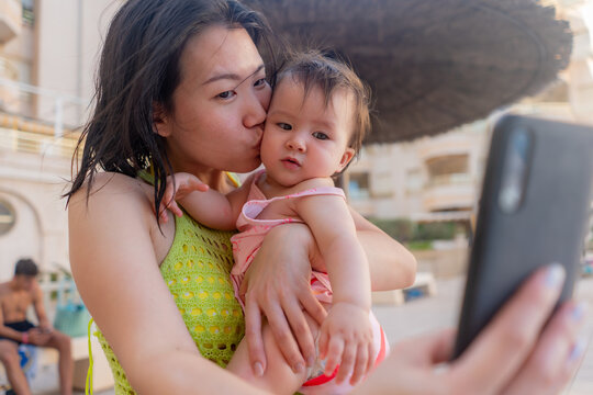 Asian woman taking selfie photo with her adorable baby girl - beautiful Chinese mother holding her little daughter and taking picture with mobile phone during holidays