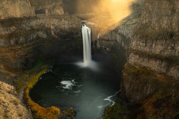 Golden Ray shines down in the morning over the Palouse Falls cascading down a rocky cliff