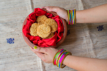 Thekua , an Indian sweet dish snacks in earthen pot . woman hand holding container in brown...