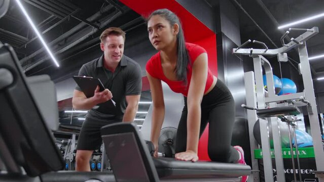 Caucasian man trainer guidance and asian woman lifting dumbbell with motivation and dedication in fitness gym, woman workout for muscular hands and arms with coach support, strength and health.