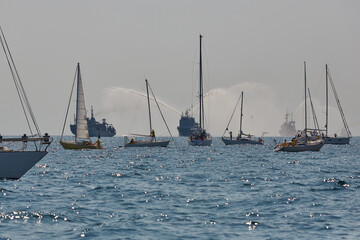 sailing yachts with warships in the background