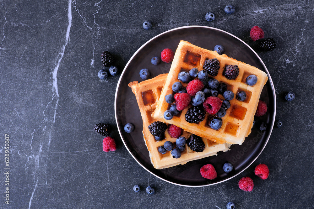 Poster breakfast waffles with raspberries and blueberries. top view over a dark stone background.
