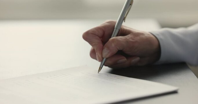 Hand of mature woman affixing signature to legal document, signing insurance medical agreement, business contract, investing to real estate property. Close up cropped shot