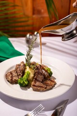 Person pouring a savory sauce onto a plate of freshly cooked steak and broccoli