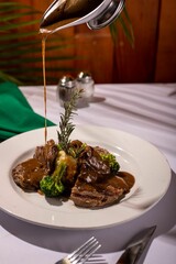 Person pouring a savory sauce onto a plate of freshly cooked steak and broccoli