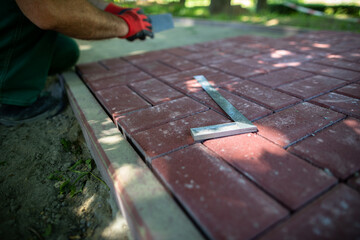 The protractor lies on the paving stones and the worker lays the pavement.
