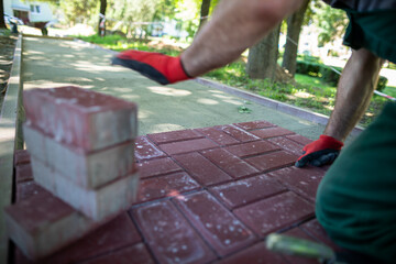 A construction worker kneels to lay paving stones on a sunny day.